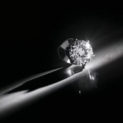 Bir tane elmas küpe siyah beyaz ve loş bir ortamda bakılırken küpenin üstüne beyaz bi ışık yansicak estetik fotoğraf